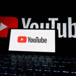 Close-up of YouTube logo displayed on a laptop screen in a dark environment.